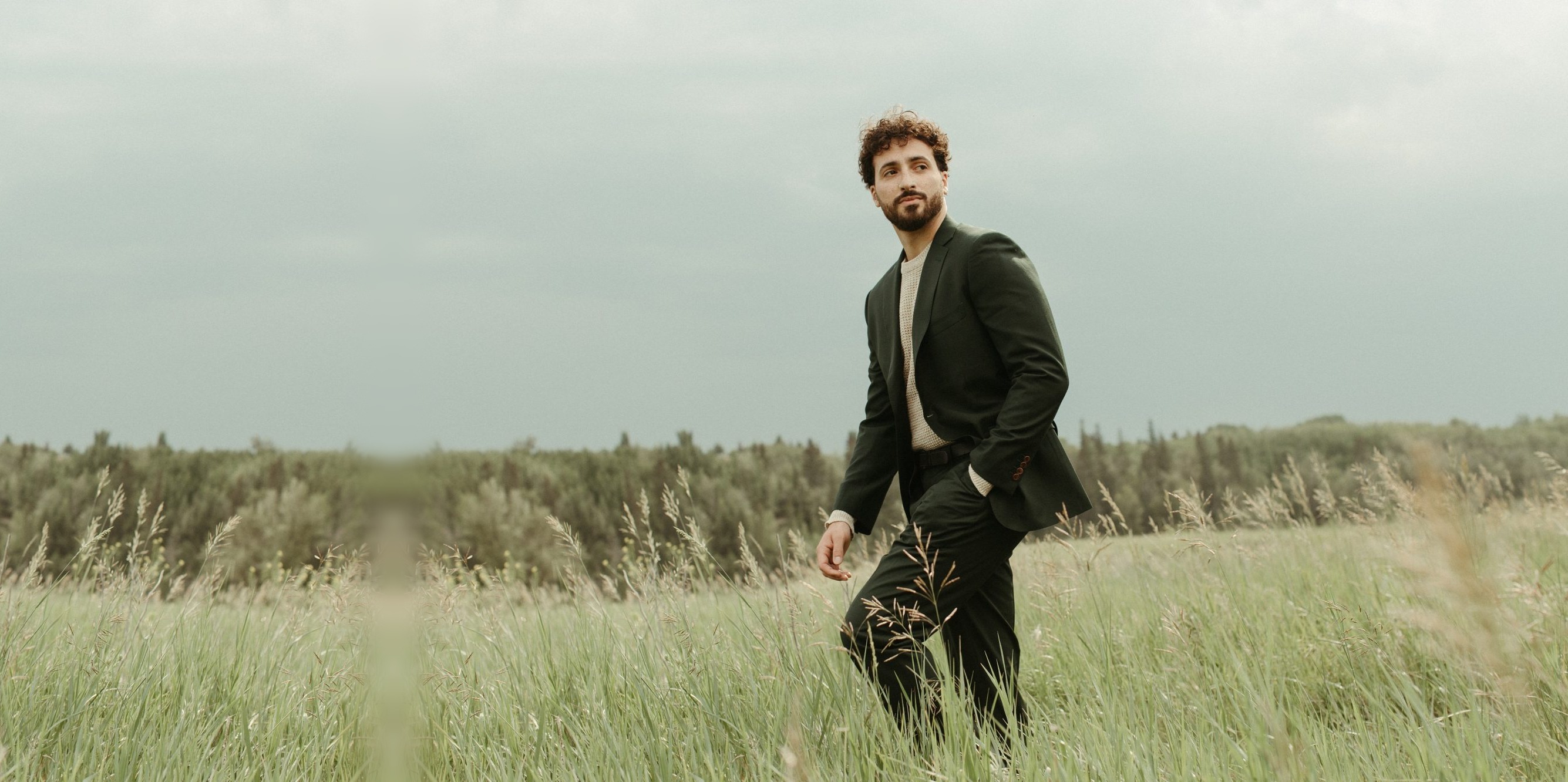 Man in a forest green James suit walking through a field